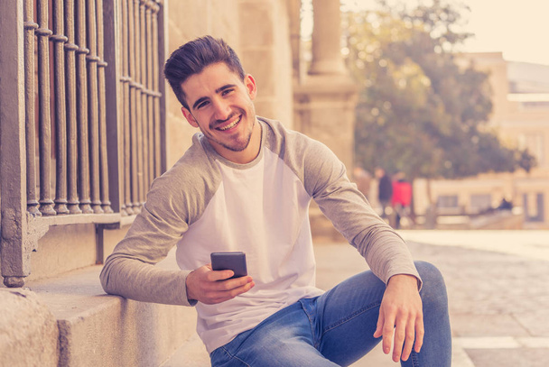Young attractive man in his twenties happy talking and chatting with friend on social media on smart phone on holidays in europe. In communication, technology internet and lifestyle concept. - Zdjęcie, obraz