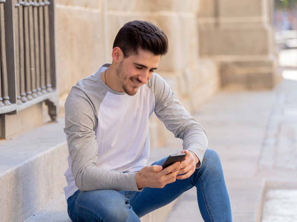 Young attractive man in his twenties happy talking and chatting with friend on social media on smart phone on holidays in europe. In communication, technology internet and lifestyle concept. - Photo, image