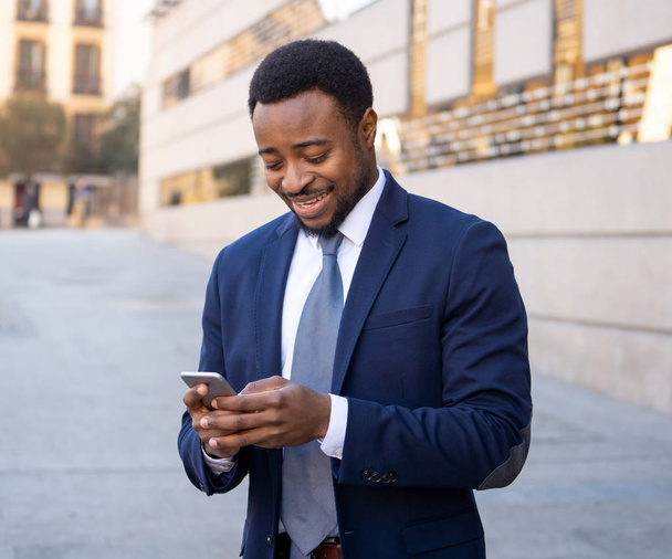 Young man in smart wear on mobile phone sending text email or social media app outdoors at city street. Happy business people, working outside, entrepreneur and work freedom communication technology. - Foto, Imagen