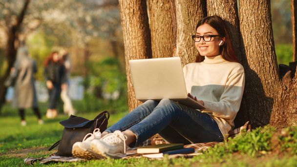 Estudante menina surf net no laptop descansando perto da árvore
 - Foto, Imagem