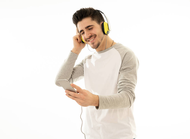 Portrait of happy young man listening to music in headphones changing songs and tracks on smartphone and singing and dancing. Isolated white background. In positive emotions, youth happiness concept. - Foto, Imagen
