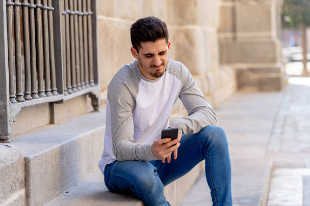 Portrait of young student man reacting negative to post in social media network or dating app with dislike showing thumb down. In social network rating likes, reactions and reassurance youth problems. - Photo, image