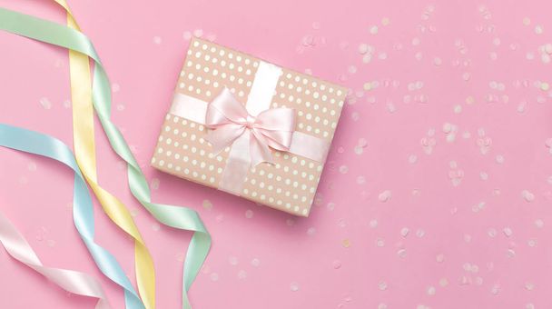 Gift or present box, beautiful festive ribbon, confetti on pink background top view. Flat lay composition for celebration, holiday, birthday Valentines Day March 8 mother day, wedding. Congratulation - 写真・画像