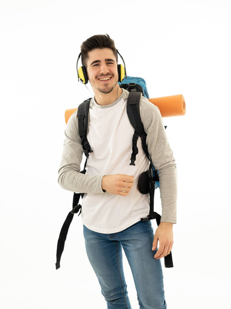 Portrait of happy young student man with backpack listening to music in headphones singing and dancing on neutral background. In positive emotions, youth traveler and happiness concept. - Фото, зображення