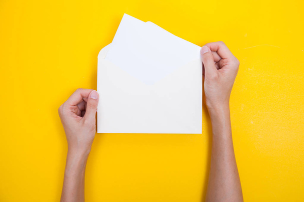 A woman hand hold a envelope and post card on yellow background - Фото, зображення