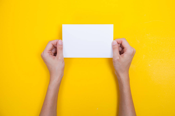 hand holding paper on a yellow background - Φωτογραφία, εικόνα