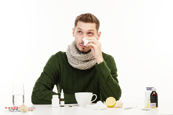 Man in a green sweater has runny nose surrounded with meds. - Foto, Imagem