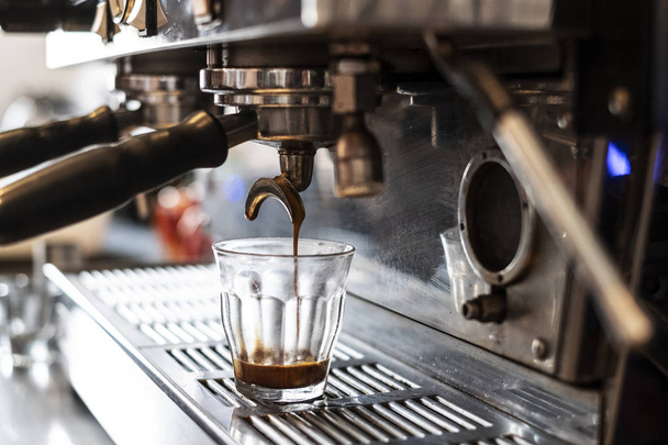 Nahaufnahme Kaffee, der in Glas auf kommerzieller Espressomaschine gegossen wird. - Foto, Bild