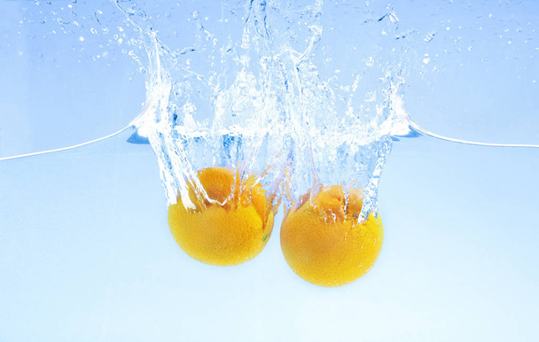 大きなスプラッシュで水の下に深く落ちる2つの熟したオレンジ - 写真・画像