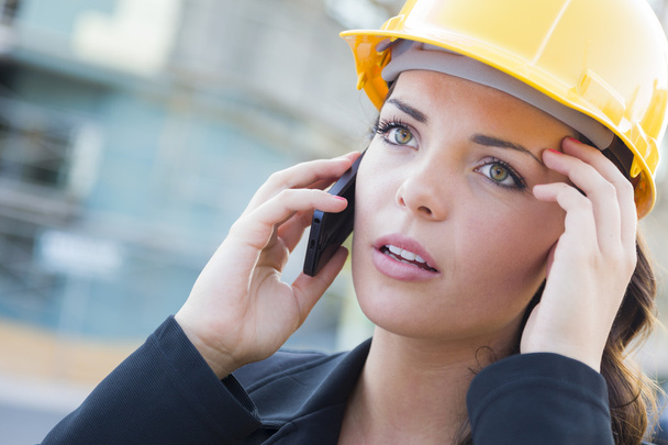 bezorgd vrouwelijke contractant helm dragen op site met behulp van de telefoon - Foto, afbeelding