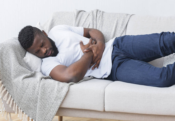 Black man suffering from stomach ache at home - Foto, Imagen