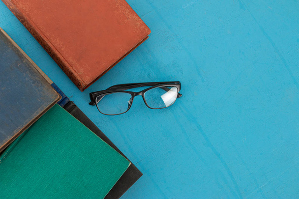 Old books and black glasses on a blue-green wooden. - Photo, Image