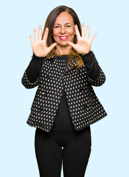 Красивая женщина среднего возраста в модной куртке показывает и указывает пальцами номер десять, улыбаясь уверенно и счастливо
. - Фото, изображение