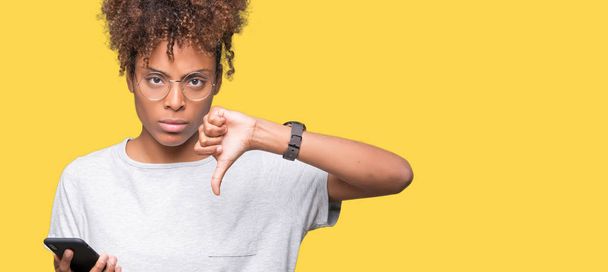 Young african american woman using smartphone over isolated background with angry face, negative sign showing dislike with thumbs down, rejection concept - Фото, изображение