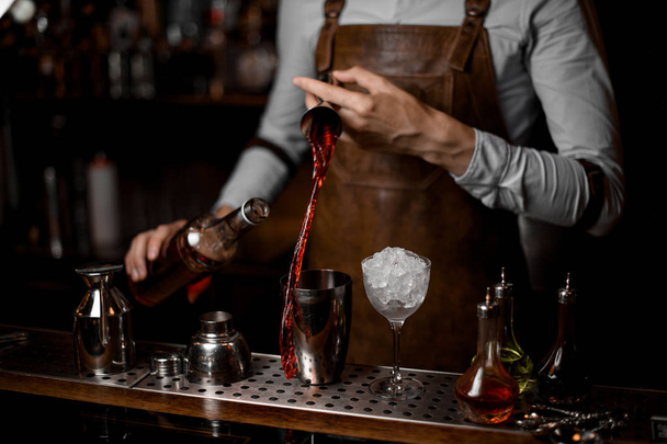 Bartender pouring a red alcoholic drink from the steel jigger to the cocktail shaker - 写真・画像