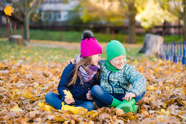 Preteen boy and girl play with yellow foliage - 写真・画像