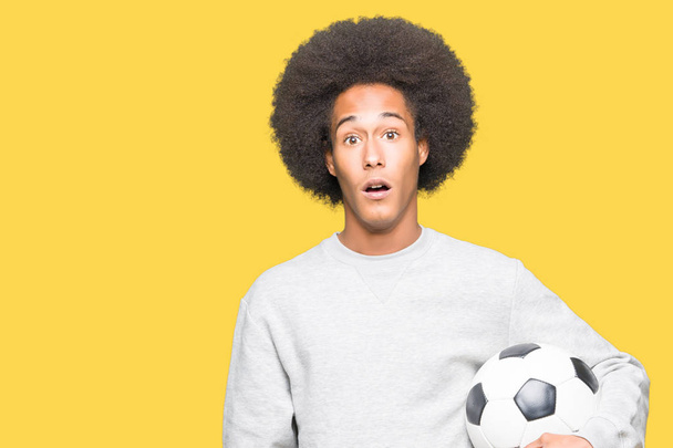 Afro-amerikai fiatalember afro haj gazdaság futball futball-labda, félek a sokk egy meglepetés arc, fél és izgatott félelem kifejezés - Fotó, kép