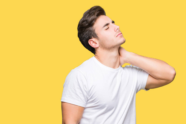 Όμορφος νεαρός φορώντας άσπρο t-shirt πάνω από το απομονωμένο φόντο δεινά του τραυματισμού του αυχένα πόνο, αγγίζει το λαιμό με το χέρι, μυϊκούς πόνους - Φωτογραφία, εικόνα