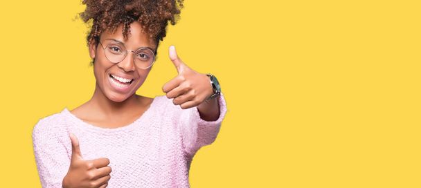 schöne junge afrikanisch-amerikanische Frau mit Brille vor isoliertem Hintergrund zustimmend positive Geste mit der Hand, Daumen nach oben lächelnd und glücklich über den Erfolg. Blick in die Kamera, Siegergeste. - Foto, Bild
