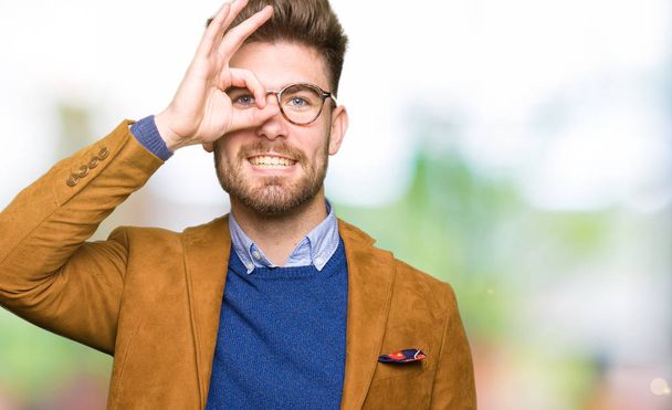 Νέοι επαγγελματίες όμορφος άνδρας φορώντας γυαλιά κάνει εντάξει χειρονομία με χέρι χαμογελώντας, μάτι αναζητούν μέσα από τα δάχτυλα με χαρούμενο πρόσωπο. - Φωτογραφία, εικόνα
