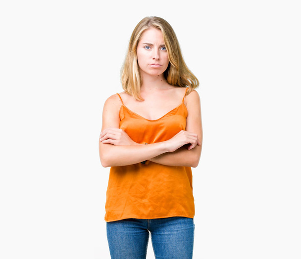 Piękna młoda kobieta pomarańczowy koszulkę na na białym tle sceptykiem i nerwowy, dezaprobaty wyraz twarzy z skrzyżowanymi rękami. Negatywne osoba. - Zdjęcie, obraz