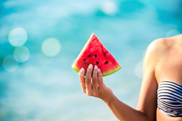 Watermelon slice in woman hand over sea - POV. Summer beach concept. Tropical fruit diet. - Foto, afbeelding