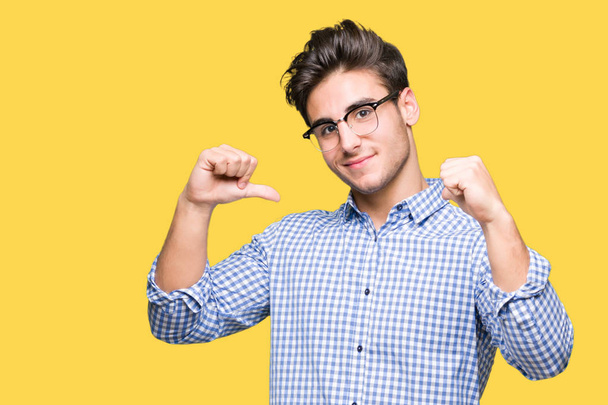Young handsome man wearing glasses over isolated background looking confident with smile on face, pointing oneself with fingers proud and happy. - Photo, Image