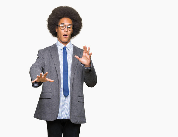 Young african american business man with afro hair wearing glasses afraid and terrified with fear expression stop gesture with hands, shouting in shock. Panic concept. - Photo, Image