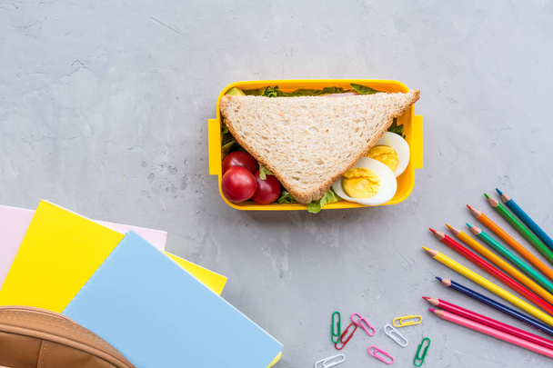 School supplies and lunch box with sandwich and vegetables. Back to school. Healthy eating habits concept - background layout with free text space. Flat lay composition, mockup, top view - Photo, Image