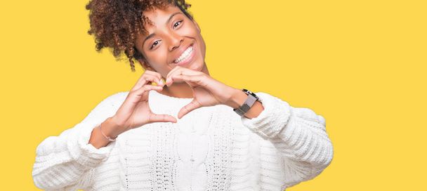 Mooie jonge african american vrouw winter trui dragen over geïsoleerde achtergrond glimlachend in liefde met hartsymbool en vorm met de handen. Romantische concept. - Foto, afbeelding