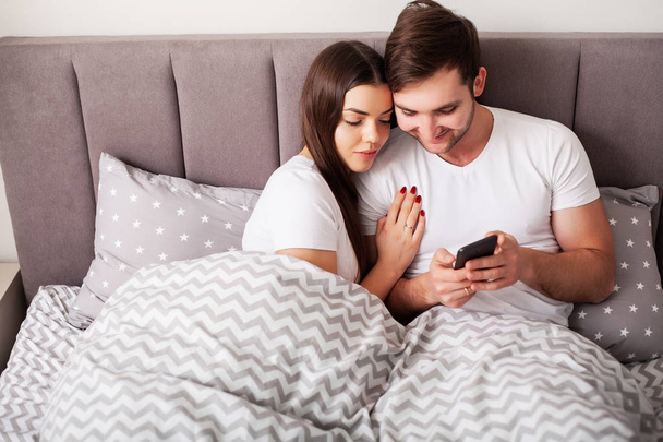 улыбающаяся молодая пара делает селфи вместе в спальне
 - Фото, изображение