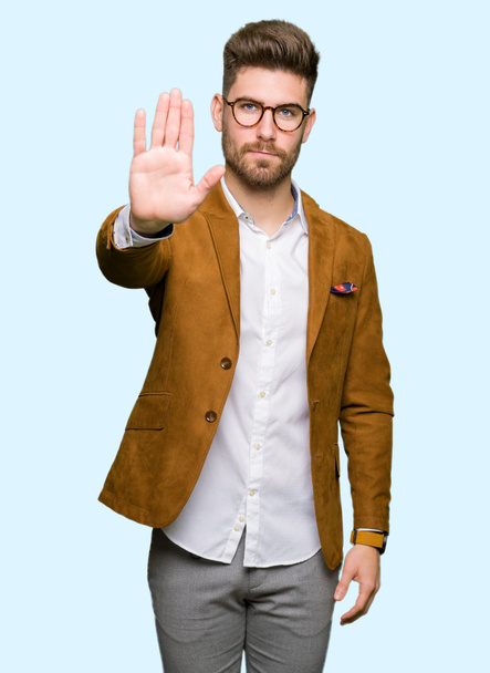 Młody przystojny biznes człowiek w okularach robi stop śpiewać z dłoni. Ostrzeżenie wyrażenie z negatywnych i poważne gest na twarzy. - Zdjęcie, obraz