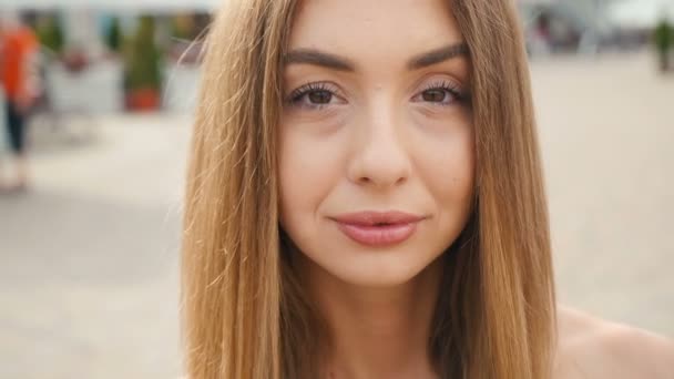 Face light brown haired young woman looking at camera close up. Portrait beautiful woman on urban city street background. - Кадри, відео