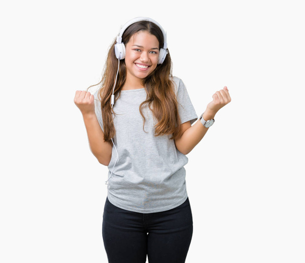 Young beautiful woman wearing headphones listening to music over isolated background celebrating surprised and amazed for success with arms raised and open eyes. Winner concept. - Valokuva, kuva