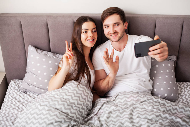 улыбающаяся молодая пара делает селфи вместе в спальне
 - Фото, изображение