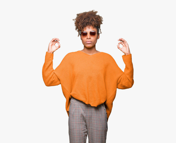 Beautiful young african american woman wearing sunglasses over isolated background relax and smiling with eyes closed doing meditation gesture with fingers. Yoga concept. - Foto, afbeelding