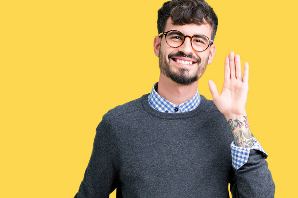 Young handsome smart man wearing glasses over isolated background Waiving saying hello happy and smiling, friendly welcome gesture - Photo, Image