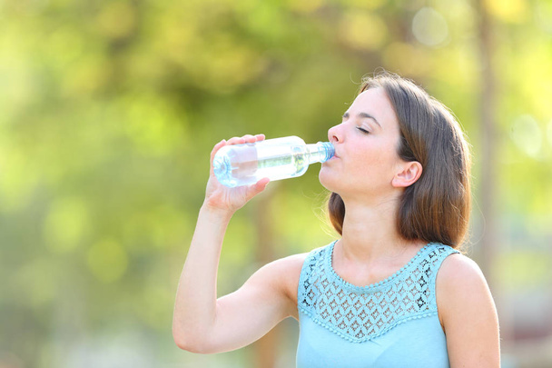 Casual vrouw drinken gebotteld water in een park - Foto, afbeelding