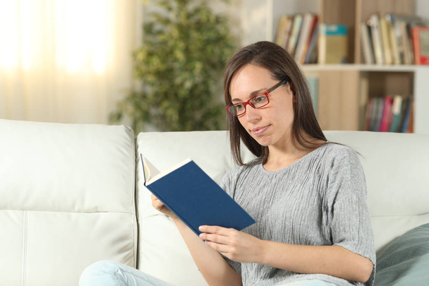 Serious woman wearing eyeglasses at home reading a book - Foto, Imagem