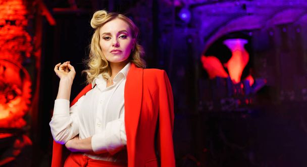 Portrait of young blonde in red suit looking at camera in nightclub - Zdjęcie, obraz