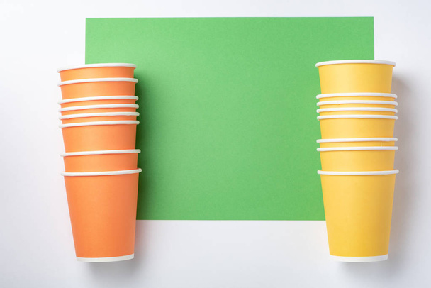 Оранжевые и желтые бумажные чашки на белом и зеленом фоне
 - Фото, изображение