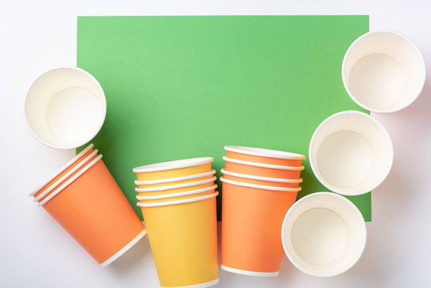 Oranžová a žlutá papírová pohárky na bílém a zeleném pozadí - Fotografie, Obrázek