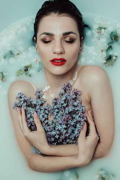 young sexy Caucasian girl with a bouquet of lilacs in the bath with milk and flowers - Photo, Image