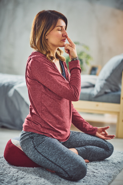 Gyönyörű kaukázusi barna ül a lótusz jóga pózol és gyakorló légzés. Hálószoba belső, reggeli rutin. - Fotó, kép