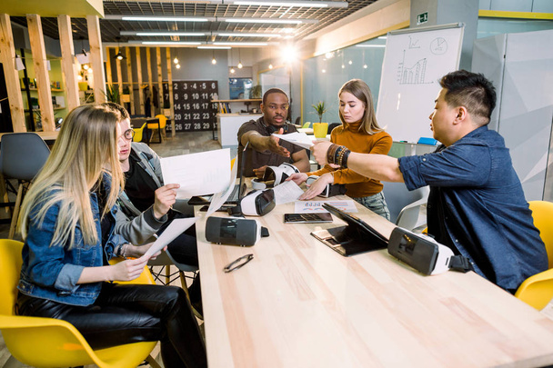Teamwork trying devices and virtual reality glasses for work in creative office. Five diverse young people using new technology at startup. Trends , social and business concept - Foto, imagen