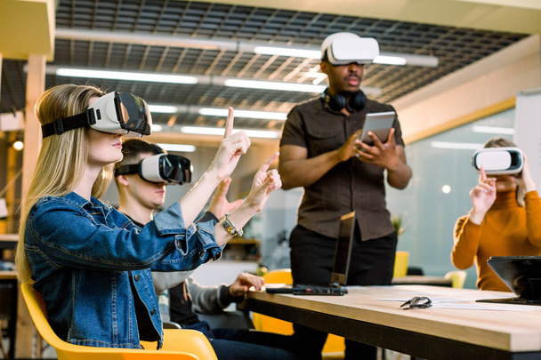 Group of positive colleagues testing virtual reality glasses. Handsome African businessman developing a project using virtual reality goggles. - Foto, Imagen
