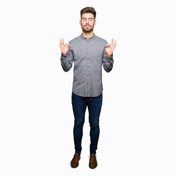 Young handsome business casual man relax and smiling with eyes closed doing meditation gesture with fingers. Yoga concept. - Photo, Image