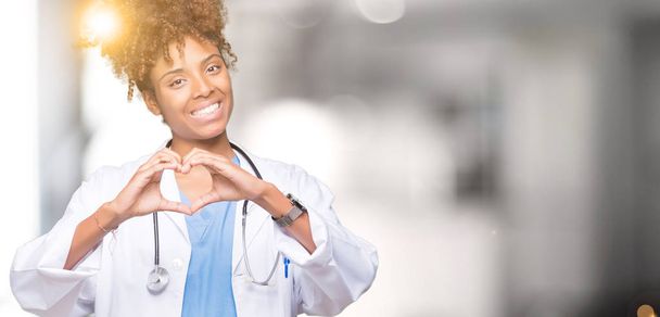 Joven mujer médica afroamericana sobre fondo aislado sonriendo en el amor mostrando el símbolo del corazón y la forma con las manos. Concepto romántico
. - Foto, Imagen