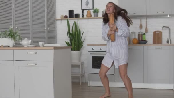 A young woman in a nightie is dancing merrily in the kitchen with a loaf of bread - Video, Çekim