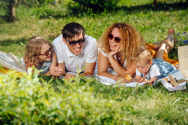 Piknik rodzinny na trawie w ogrodach pod delikatnym odcieniem drzew - Zdjęcie, obraz